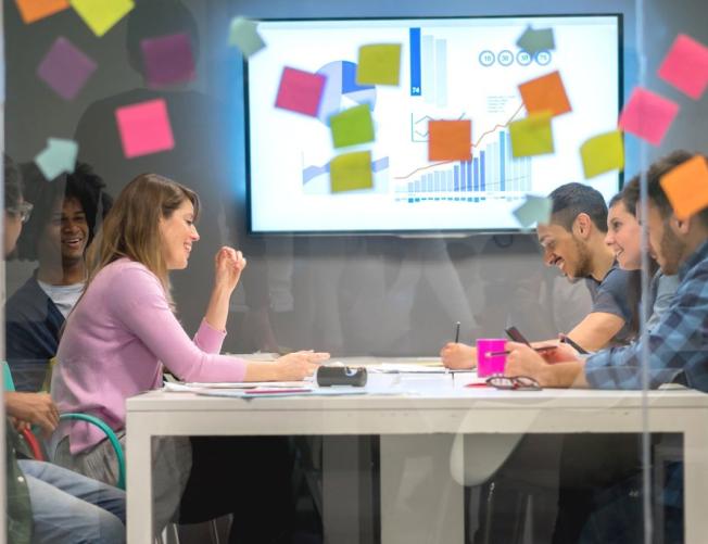 a group of people in a glass office with colorful Post-its p