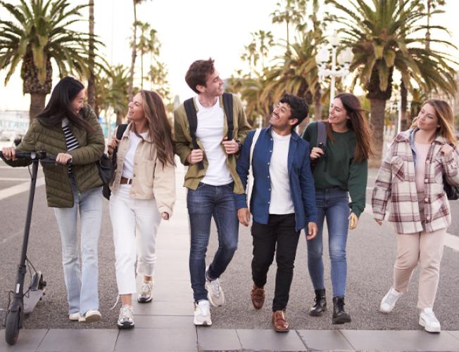 Multicultural group of millennial friends walking along street with palm trees.