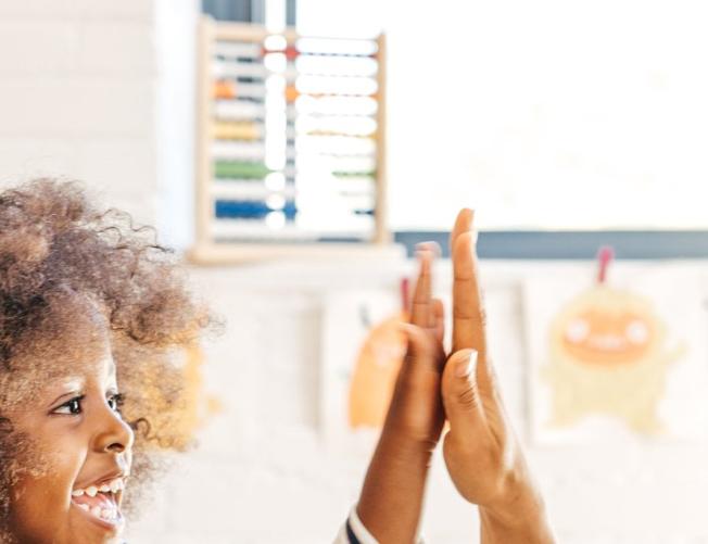 teacher high-fiving a little girl while they stack blocks to
