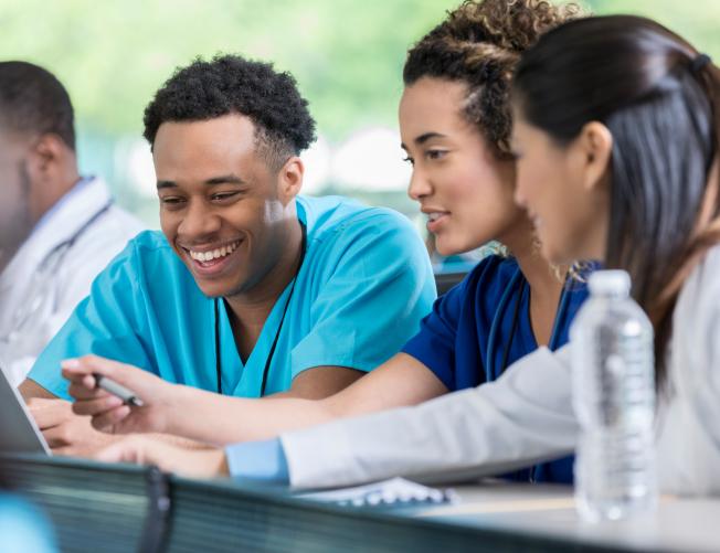 Diverse male and female nursing students review information for a test. They are looking at a laptop.