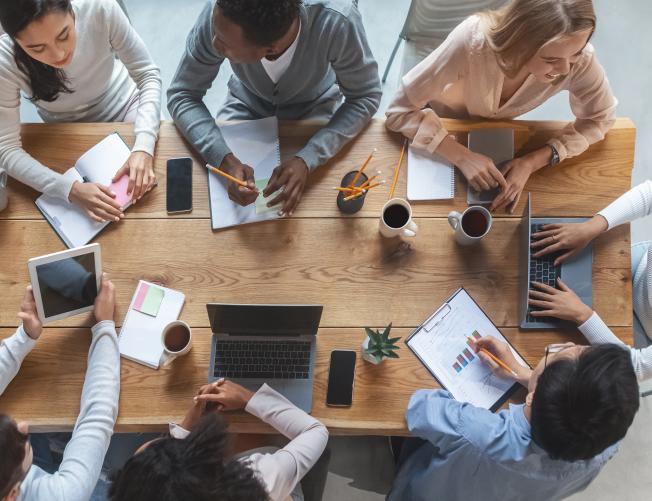Office lifestyle concept. Top view of international young business team having meeting at office, sitting around table
