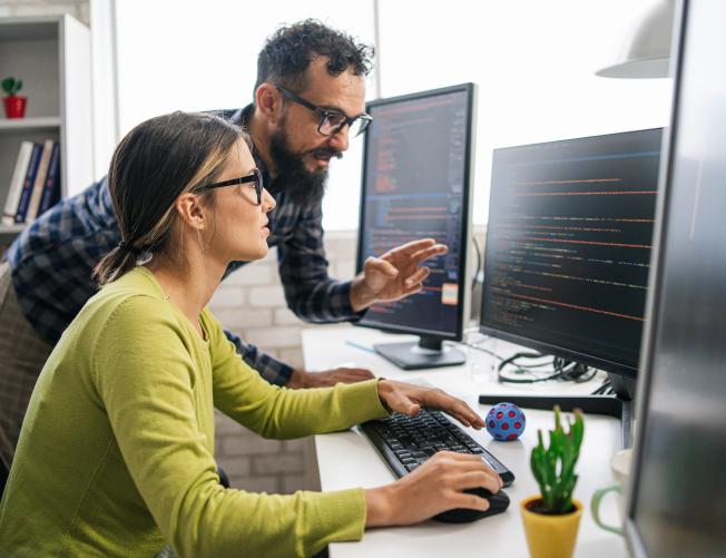 oman working on a computer with a man looking at the screen and either teacher her or learning from her.