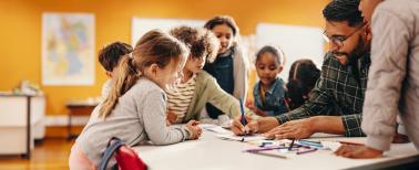 Teacher showing students how to draw using a color pencil around a table