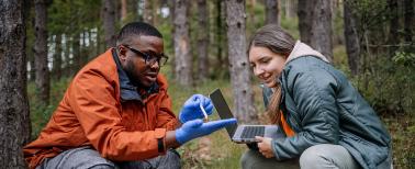 biologist explaining project to a science writer outdoors in a forest.