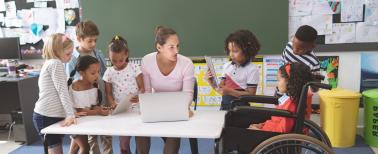 Students using digital tablet while teacher interacting with students in classroom at school