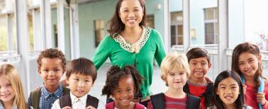 teacher and eight small children facing the camera, outside 