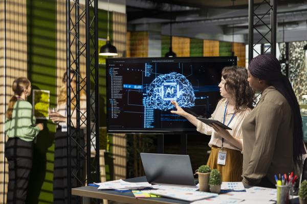 Two women in an office looking at a monitor with an AI image on it