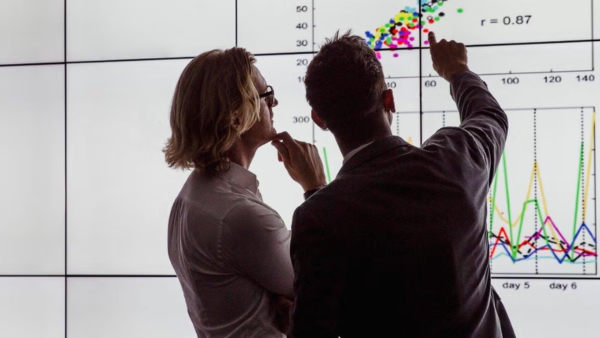 Two people looking at a white screen with charts. 