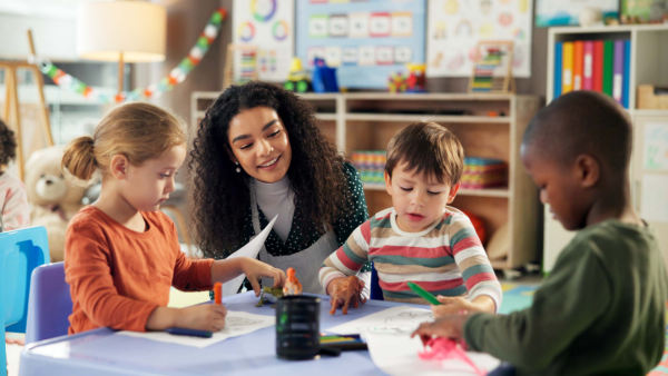 Three students playing at a table with a teacher looking on.